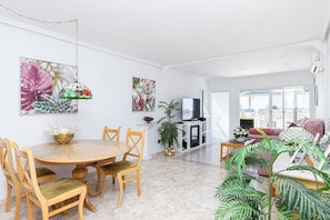 A spacious living room with a dining area, a TV, and a balcony with a view. - Charming Bungalow With Ocean Views in Roquetas de Mar (Roquetas de Mar)