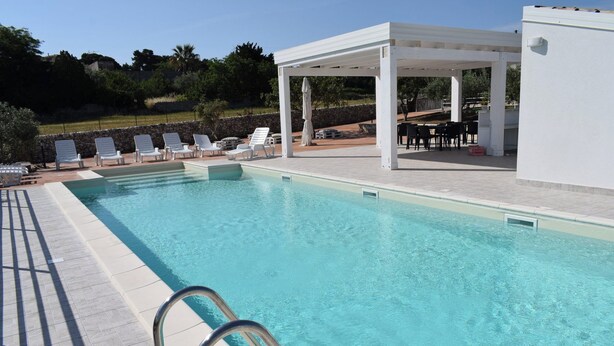 A clear swimming pool with lounge chairs and a covered seating area. - CrauNari Agritourism and Educational Company (Modica)