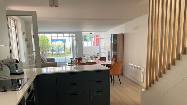 A modern kitchen with a central island, a dining area with chairs, and a staircase. - Villa Mandarine (Arcachon)