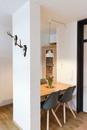 Uma sala de jantar com uma mesa de madeira, cadeiras pretas, um vaso com flores e um cabeça de veado presa na parede.