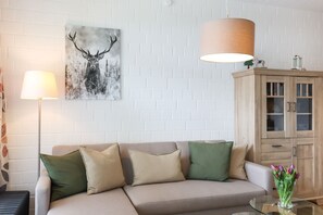 Un salon comprenant un canapé, des lampes, un meuble et une œuvre d’art représentant un cerf, accrochée au mur.