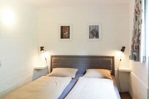 Ein Doppelbett mit Kopfteil, zwei Nachttische mit Lampen und zwei gerahmte Bilder an der Wand.