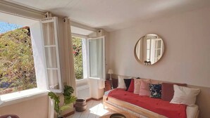 A room with a sofa, a small table, a mirror, and a window with curtains. - La maison du repos (Hyères)