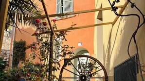 A courtyard with a wooden bench, a metal table, a large wheel, and potted plants. - La maison du repos (Hyères)