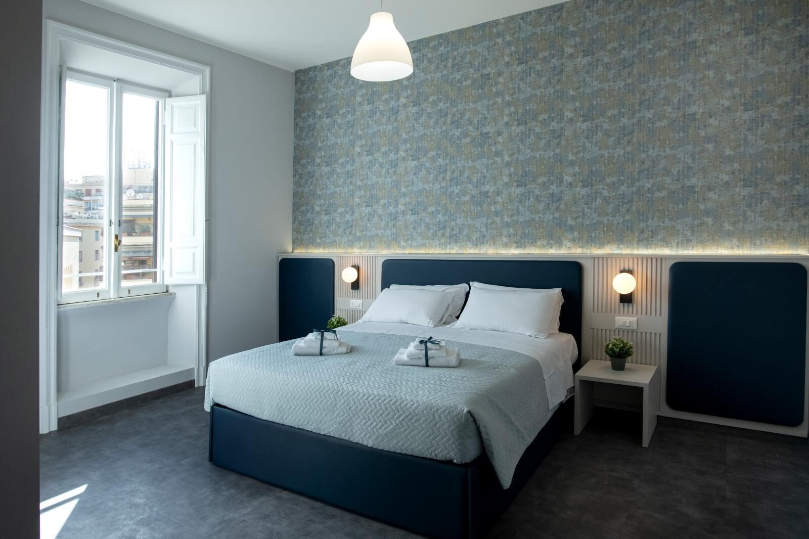 A modern bedroom with a large bed, bedside tables, a window, and a patterned wall.