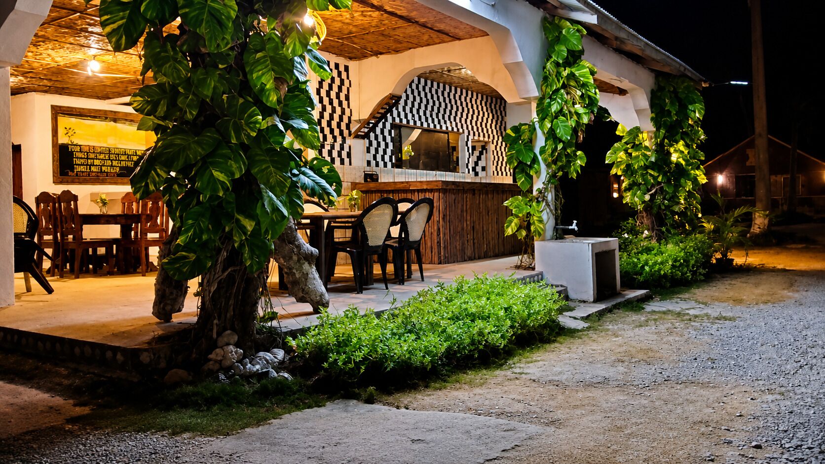 Un espacio exterior para comer con mesas y sillas, una pérgola de madera y un diseño de pared a cuadros.