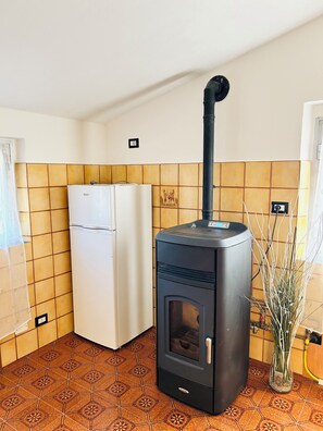Eine Küche mit einem schwarzen Holzofen, einem weißen Kühlschrank und gemusterten Fliesen.