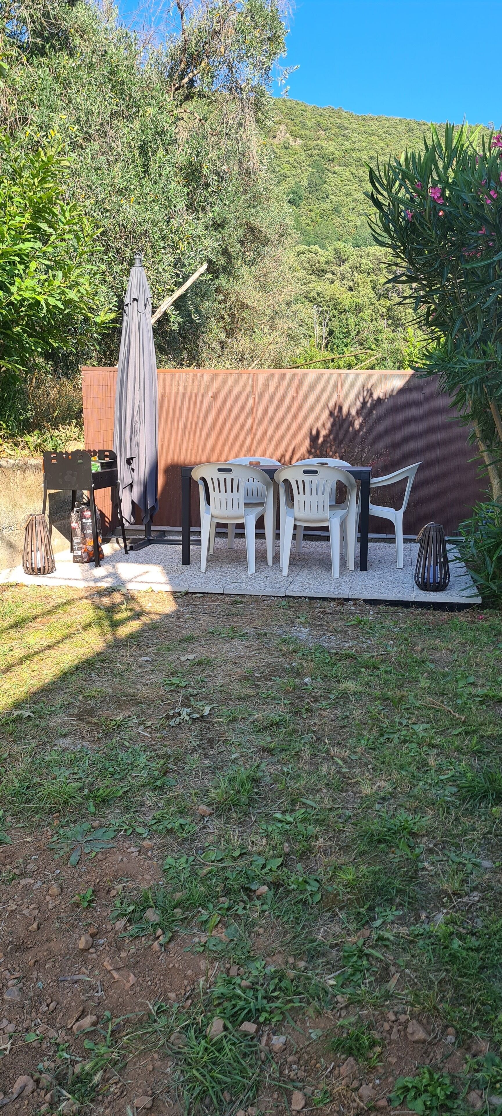 Un espace extérieur aménagé avec des chaises en plastique et une table, un parasol et une clôture en bois en arrière-plan.
