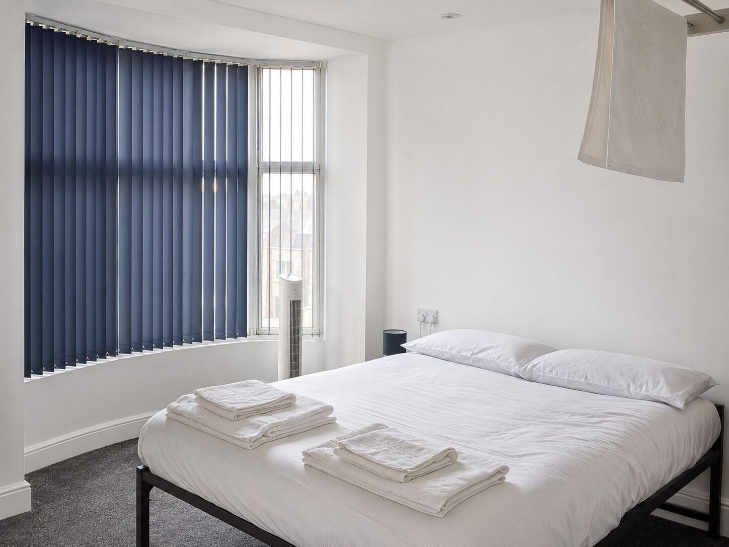 Ein Schlafzimmer mit einem Bett, zwei Kissen, einem Fenster mit blauen Vorhängen und einem Nachttisch mit einer Lampe.