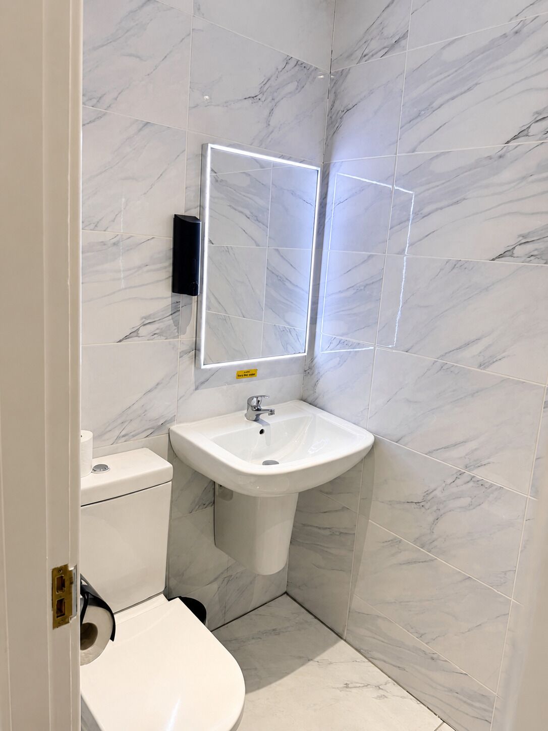 Un baño con un lavamanos blanco, un inodoro y un espejo con luz.