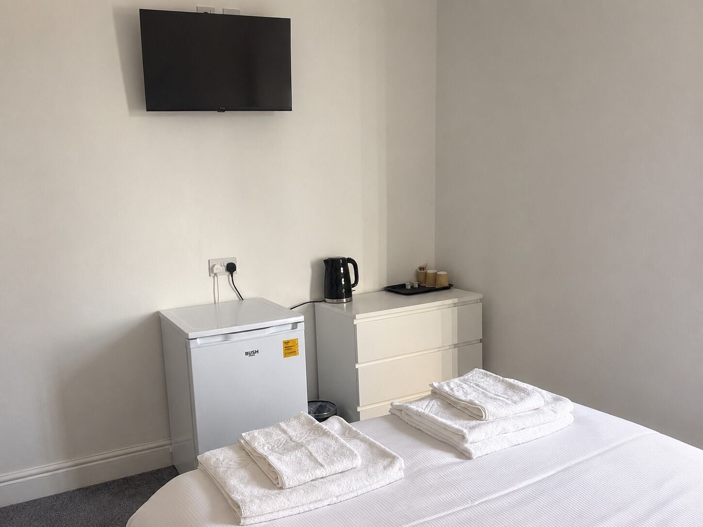 A hotel room with a bed, a small desk, a coffee maker, and a television on the wall.