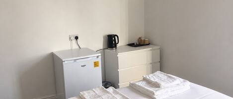 A hotel room with a bed, a small desk, a coffee maker, and a television on the wall.
