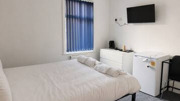A hotel room with a bed, a desk, a chair, a television, and a window with curtains.