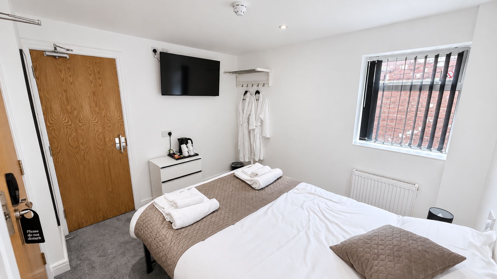 A hotel room with a bed, a television, a window with bars, a radiator, and a door with a 'Please do not disturb' sign.