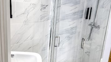 Un baño moderno con ducha envuelta en vidrio, lavamanos blanco y un inodoro.