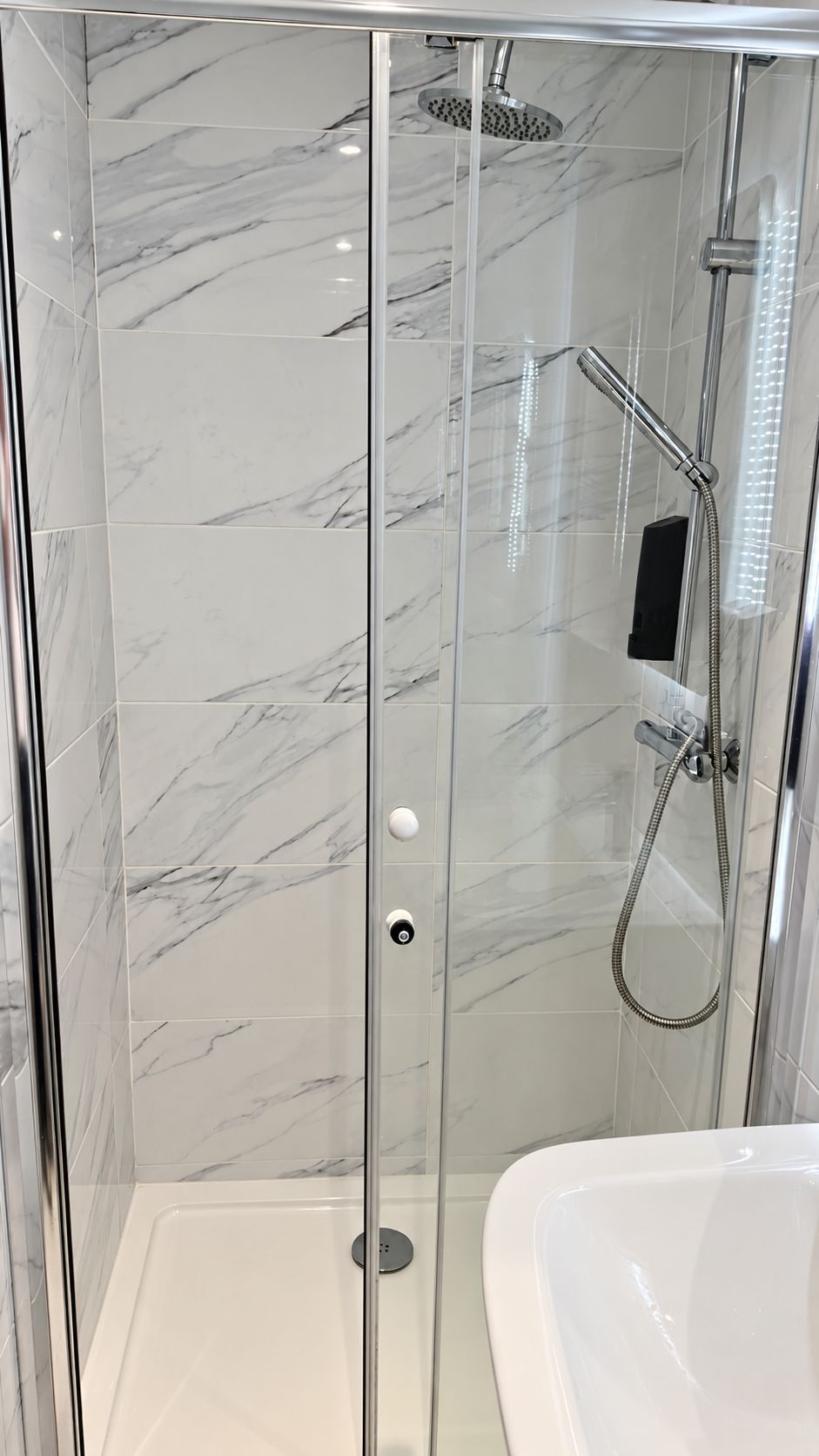 A glass-enclosed shower with a handheld showerhead and a wall-mounted faucet.