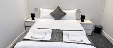 Une chambre d’hôtel avec un lit, deux tables de chevet, une poubelle et un tableau encadré au mur.