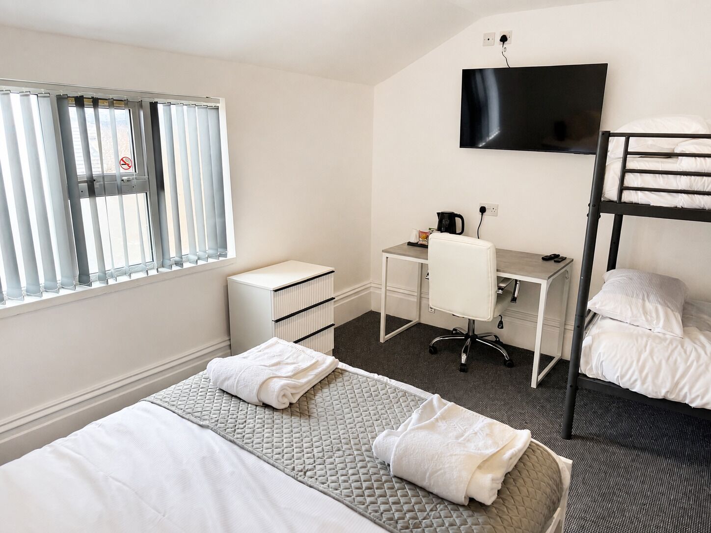 A hotel room with a bunk bed, a desk with a chair, a television, and a window with blinds.