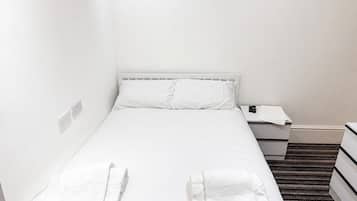 Een eenpersoonskamer met wit beddengoed, twee handdoeken, een nachtkastje met een afstandsbediening en een bedtafel.