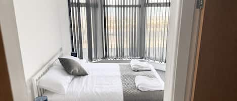 A hotel room with a bed, a nightstand, a lamp, a window with curtains, and a view of the outdoors.