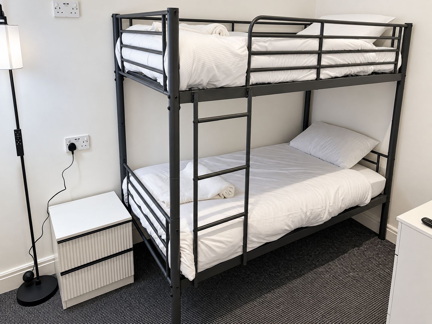 A bunk bed with a desk and a lamp, a power outlet, and a radiator.