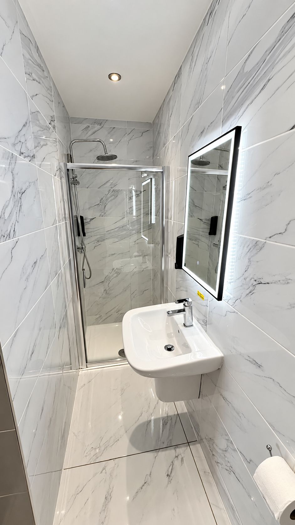 A modern bathroom with a glass-enclosed shower, a white sink, and a large mirror.