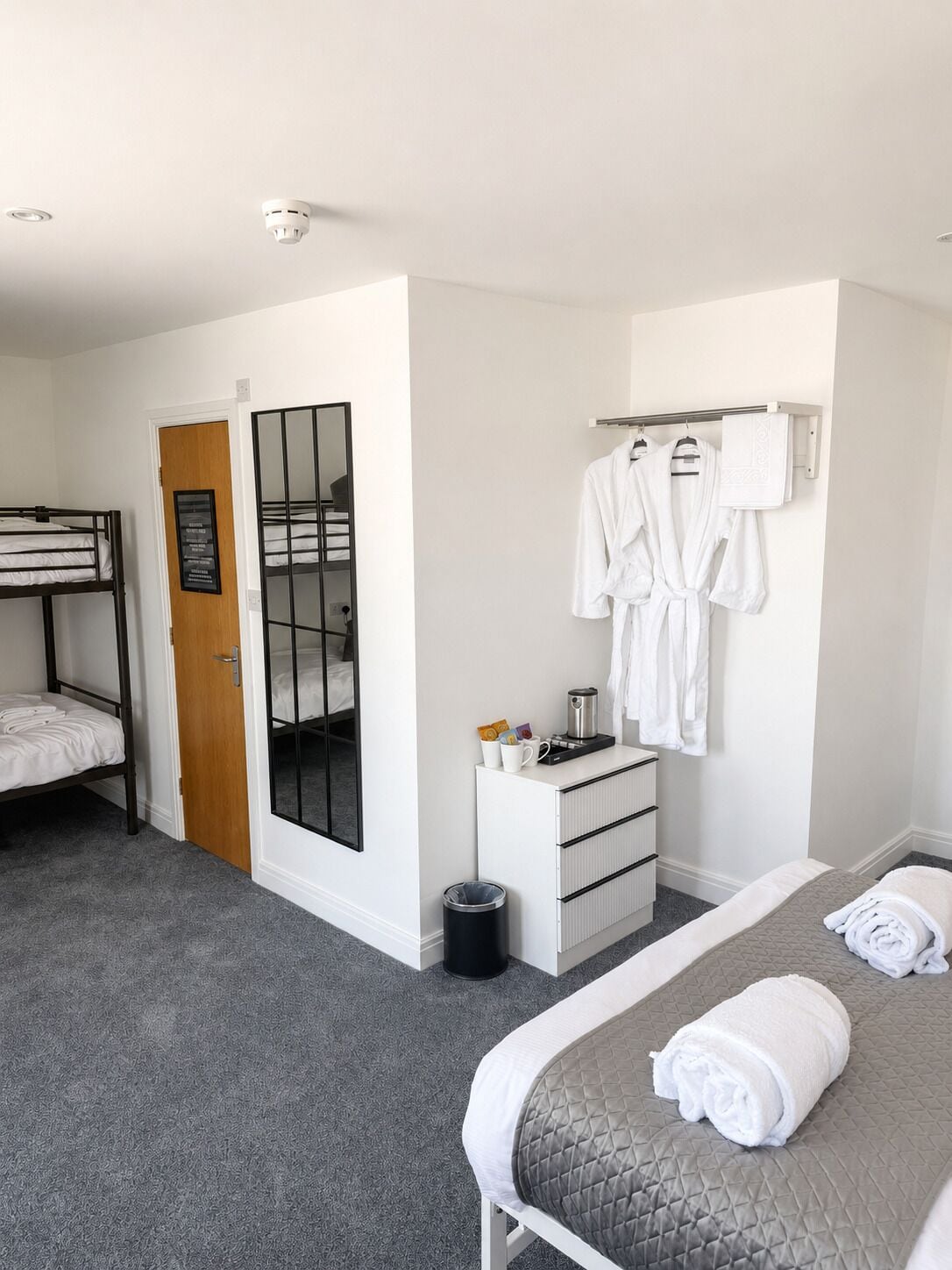 Een slaapkamer met een stapelbed, een spiegel, een nachtkastje met toiletartikelen en een net opgemaakt bed.
