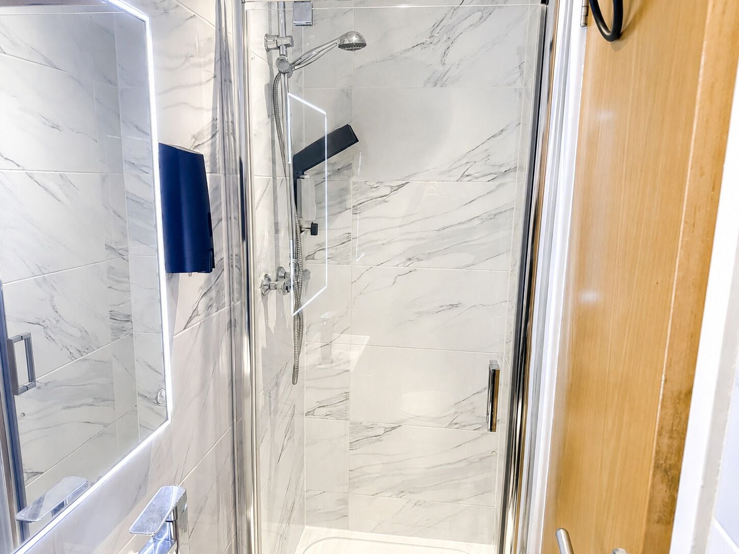 Een moderne badkamer met een douchecabine van glas, marmeren tegels en een houten deur.