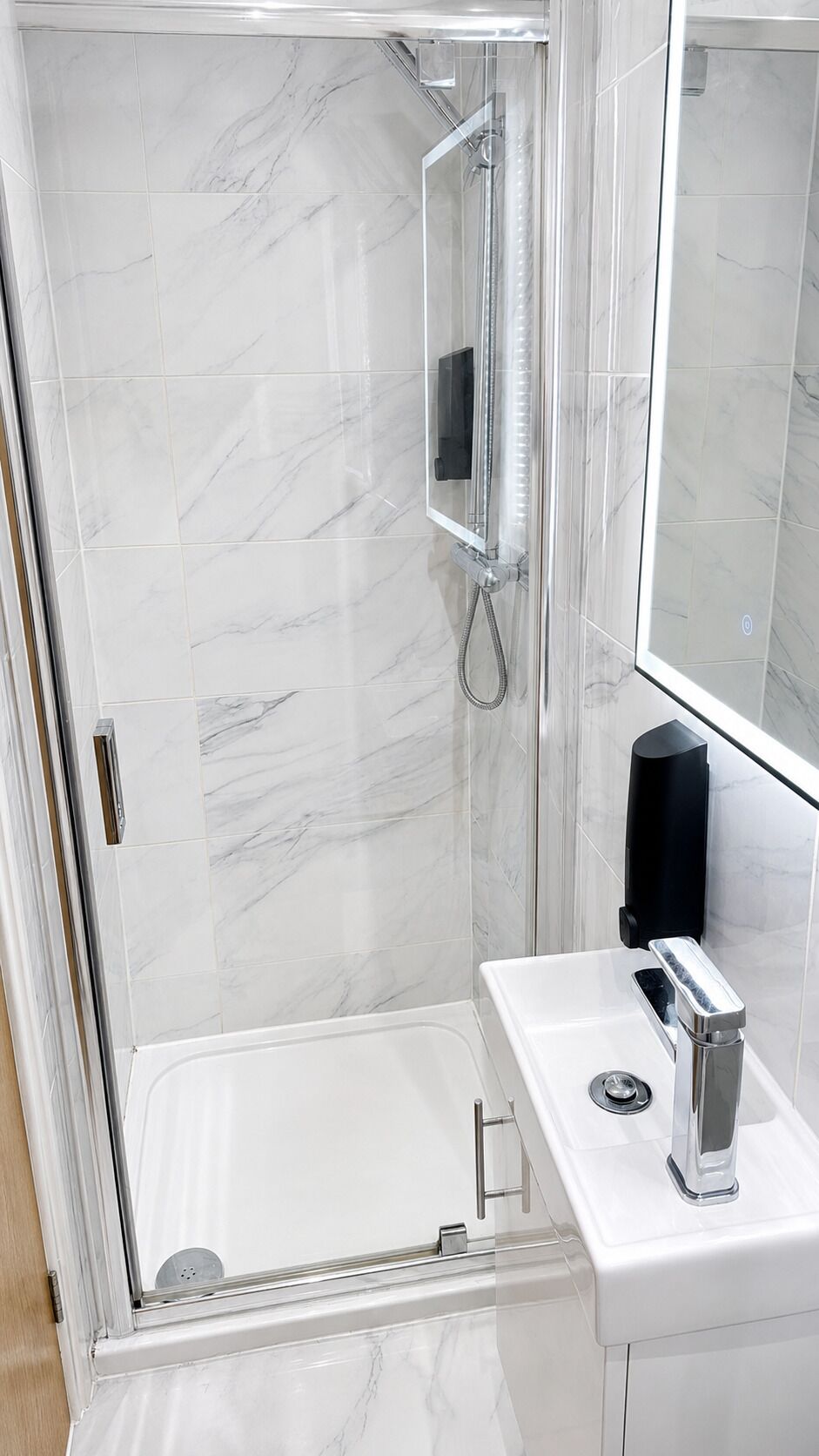 A modern bathroom with a glass-enclosed shower, a white sink with a chrome faucet, and a large mirror.