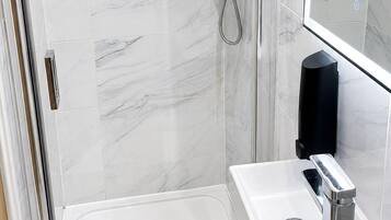 A modern bathroom with a glass-enclosed shower, a white sink with a chrome faucet, and a large mirror.
