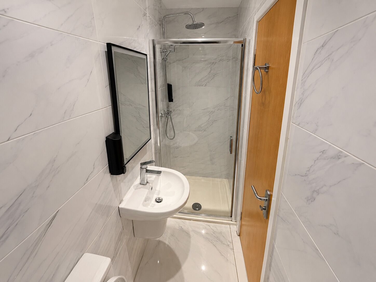 Un baño moderno con ducha de mampara de vidrio, lavamanos pedestal y retrete.