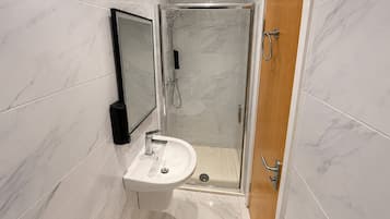 Un baño moderno con ducha de mampara de vidrio, lavamanos pedestal y retrete.