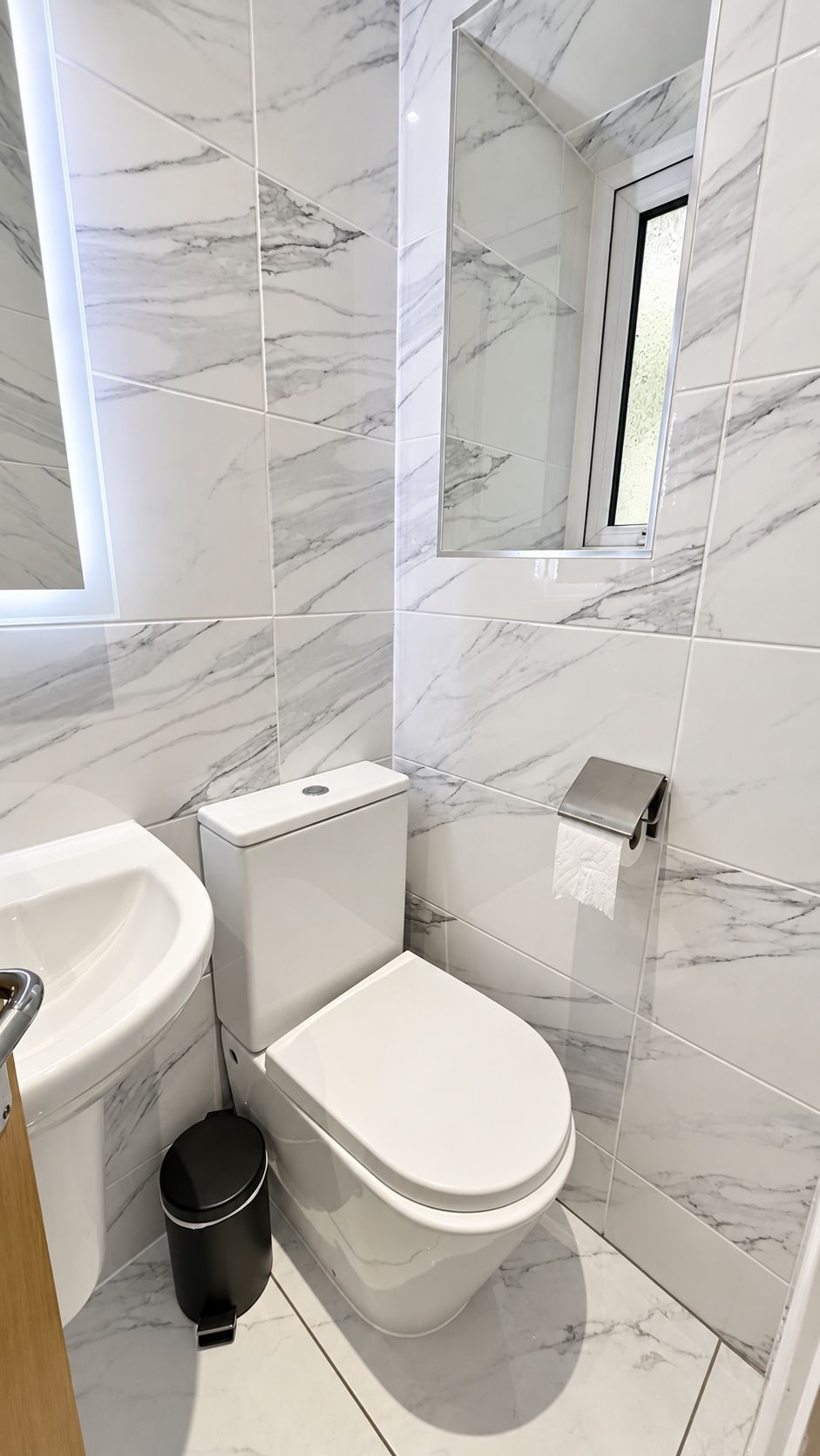 A bathroom with a toilet, sink, and trash can, all against a marble wall.
