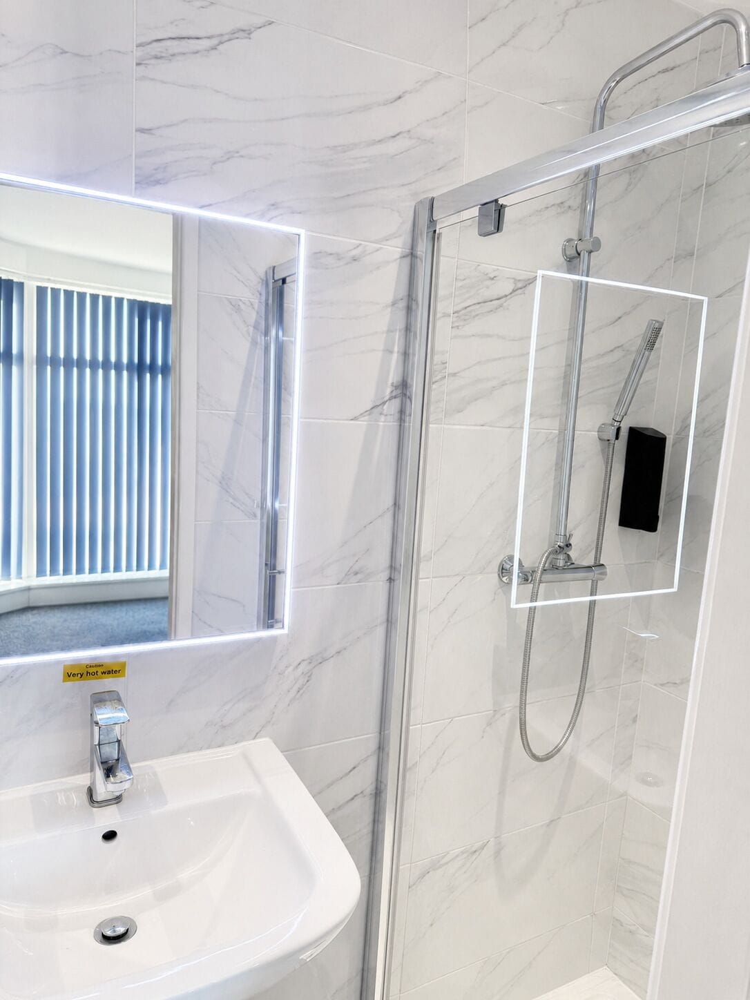 Un baño con lavamanos de mármol blanco, ducha con cerramiento de vidrio e iluminación LED en el espejo.