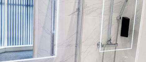Un baño con lavamanos de mármol blanco, ducha con cerramiento de vidrio e iluminación LED en el espejo.