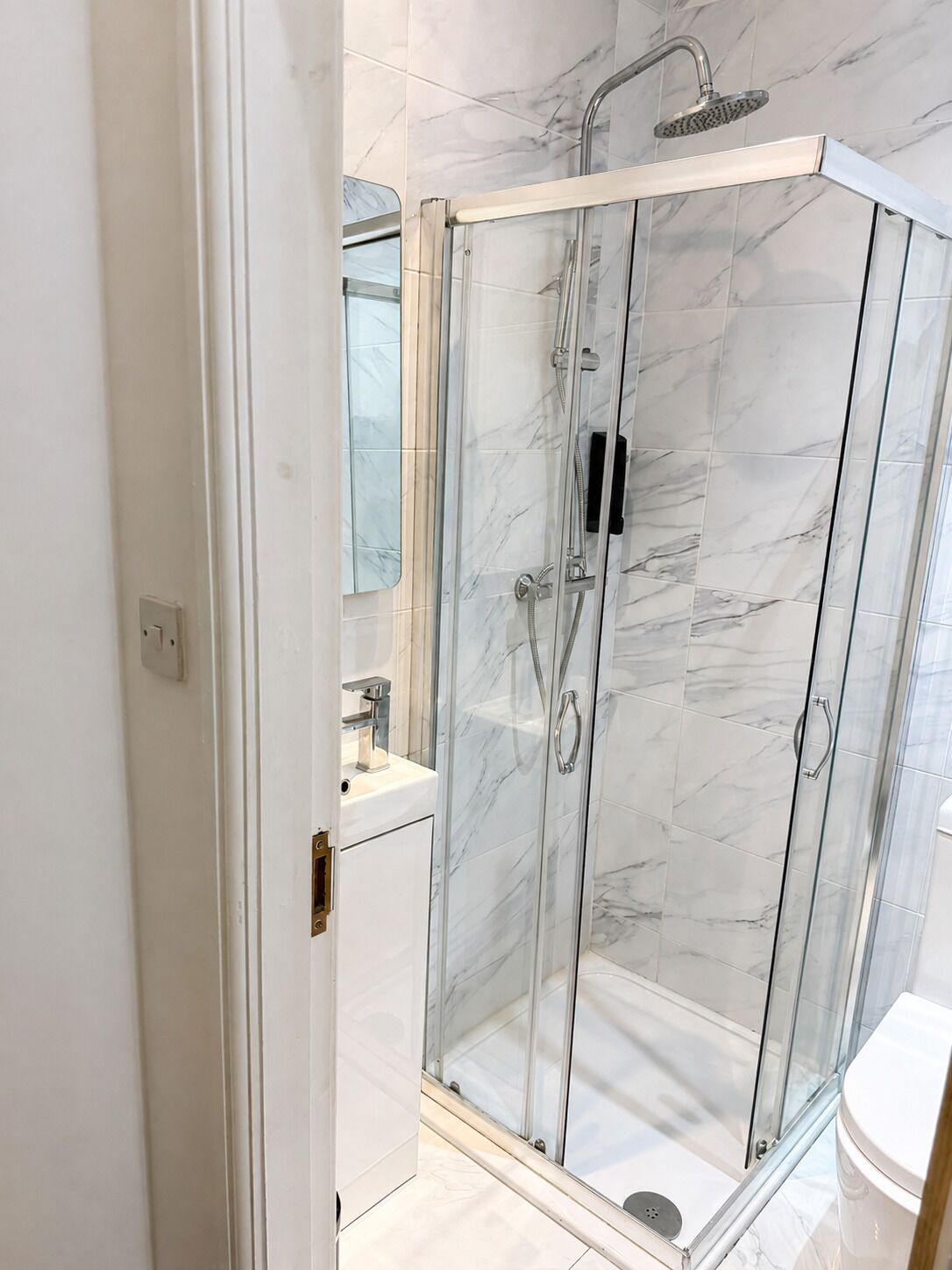 Een douche met glazen wand, een handdouche en een wandmengkraan.