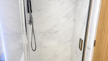 A glass-enclosed shower with a marble wall, a sink with a faucet, and a wooden door.