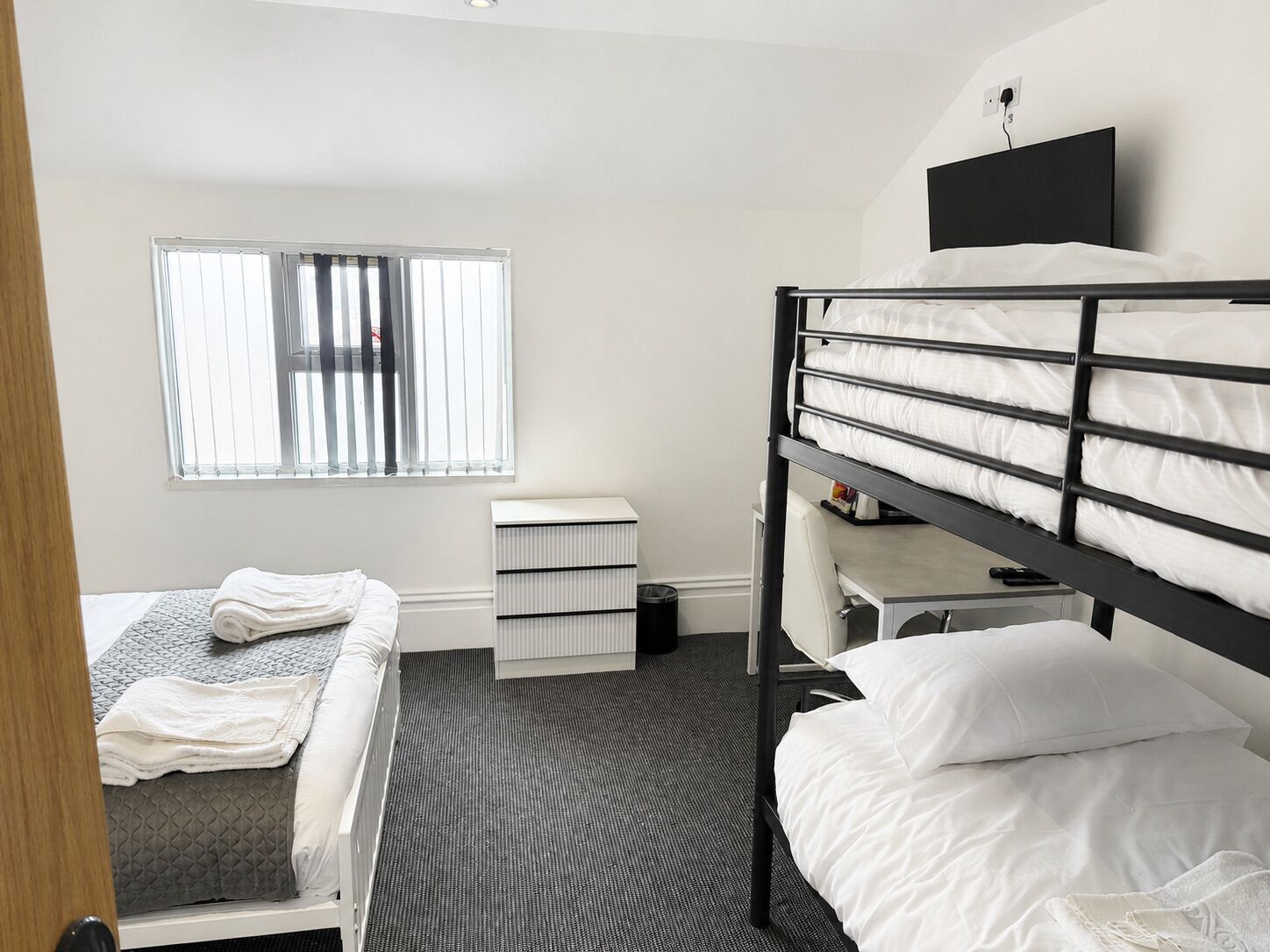 Een slaapkamer met stapelbedden, een bureau, een stoel, een radiator en een raam met jaloezieën.
