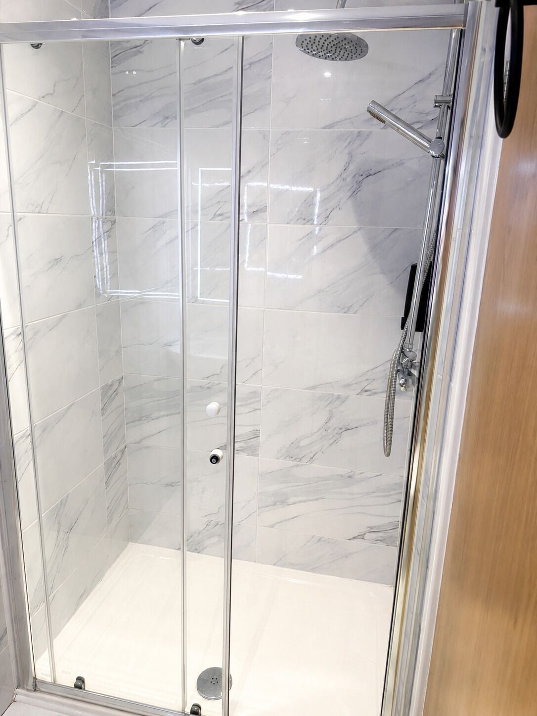 A glass-enclosed shower stall with a handheld showerhead and a wall-mounted faucet.