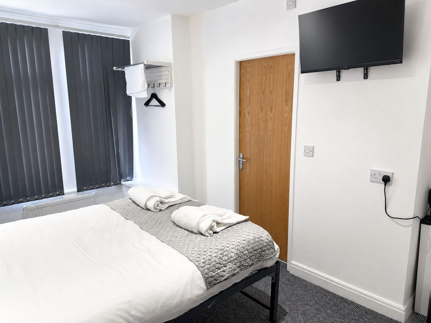 Une chambre d’hôtel avec un lit, un téléviseur fixé au mur, une porte et une fenêtre avec des stores.