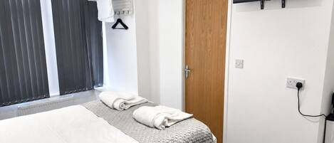 Une chambre d’hôtel avec un lit, un téléviseur fixé au mur, une porte et une fenêtre avec des stores.