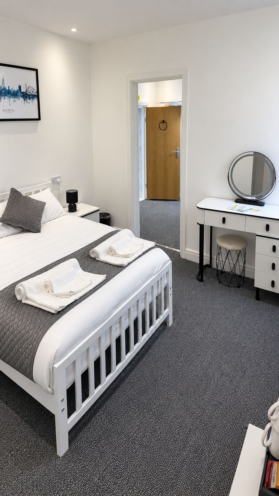 A hotel room with a bed, a desk, a chair, a mirror, and a door leading to another room.