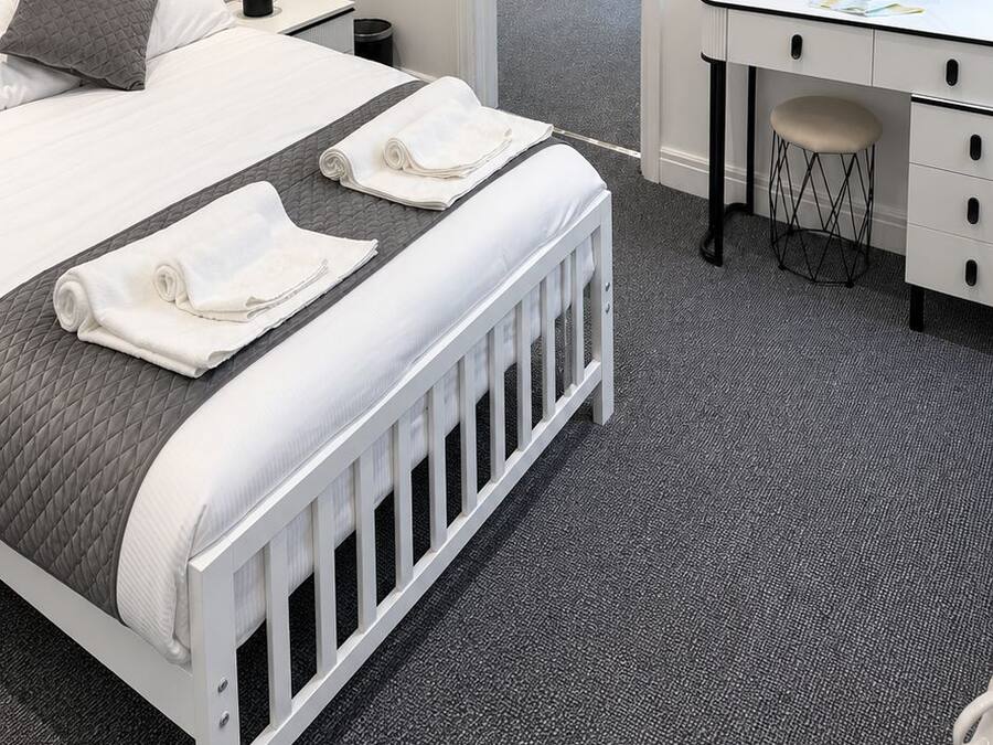 A hotel room with a bed, a desk, a chair, a mirror, and a door leading to another room.
