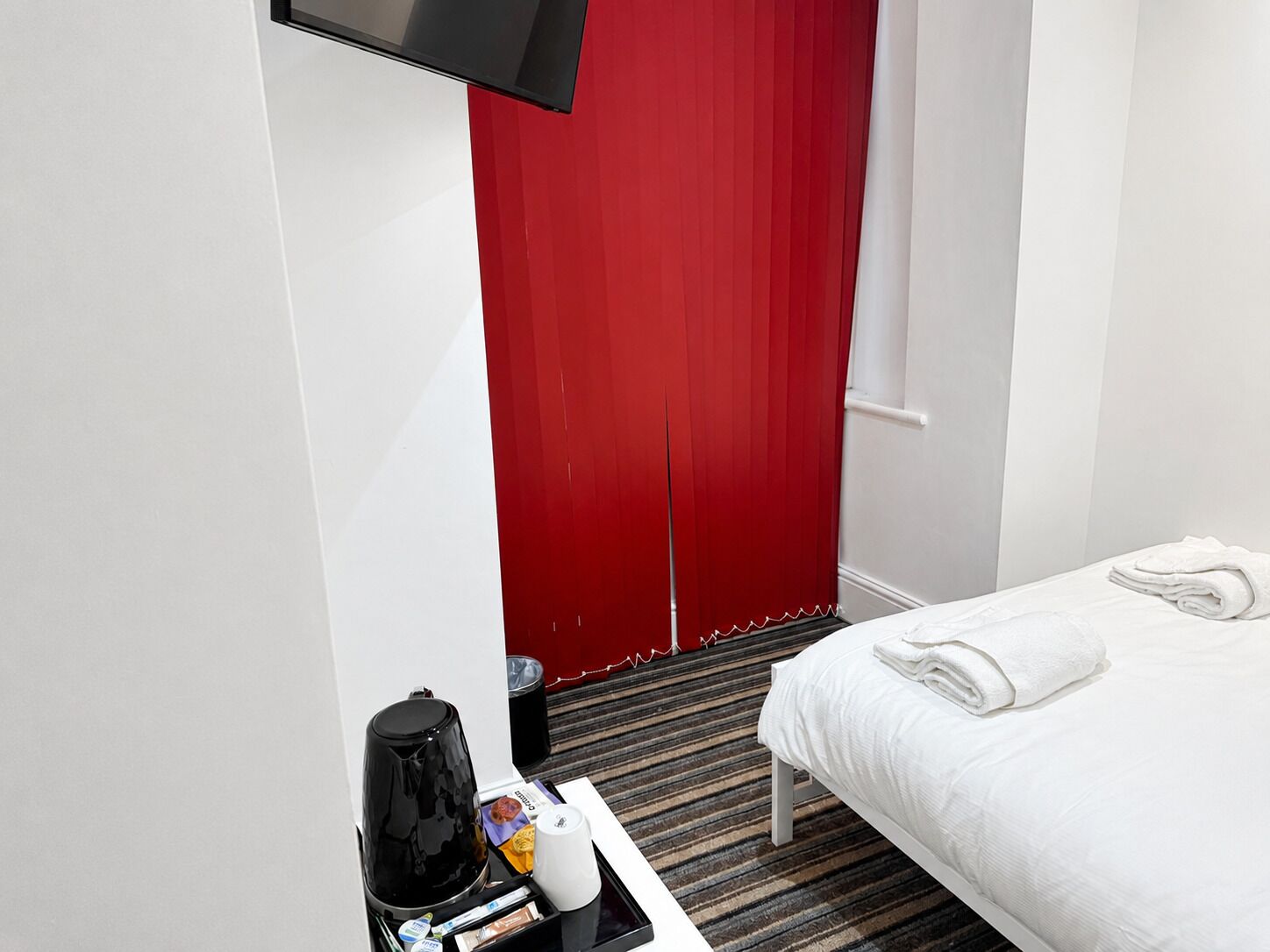 A hotel room with a bed, a coffee maker, a tray with toiletries, and a red door.