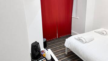 A hotel room with a bed, a coffee maker, a tray with toiletries, and a red door.