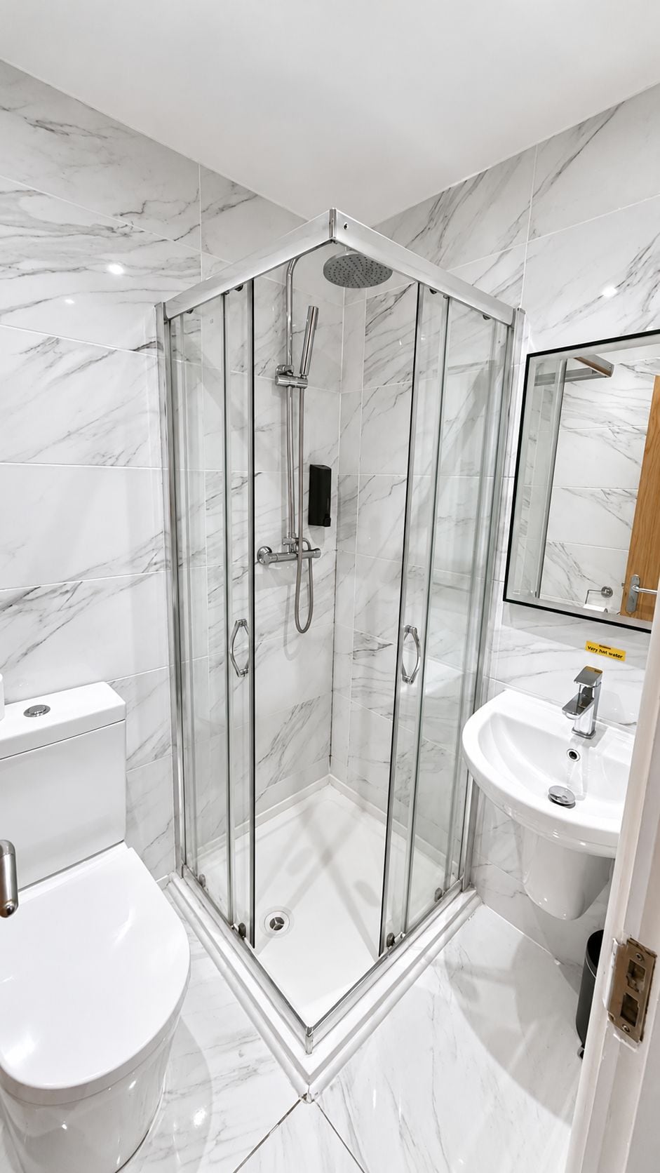 A modern bathroom with a glass-enclosed shower, a white toilet, and a sink with a mirror.