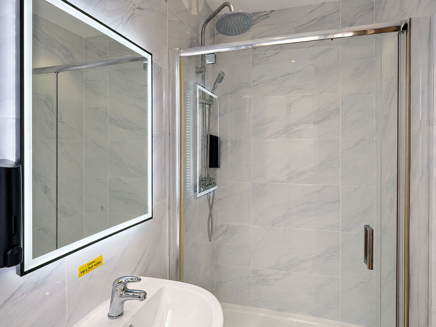 Un baño moderno con ducha envuelta en vidrio, lavamanos blanco y un espejo grande.