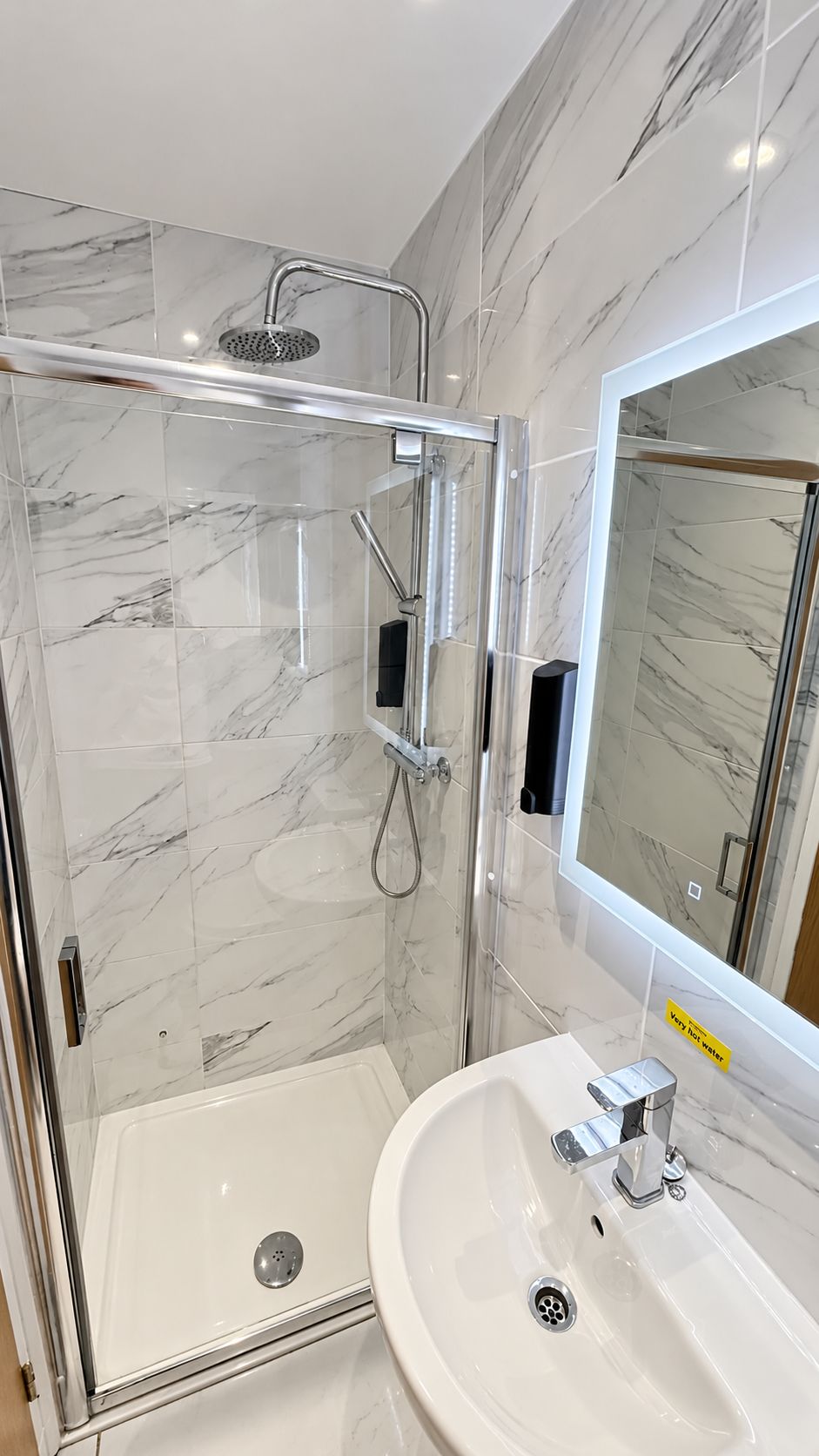A modern bathroom with a glass-enclosed shower, a white sink, and a large mirror.