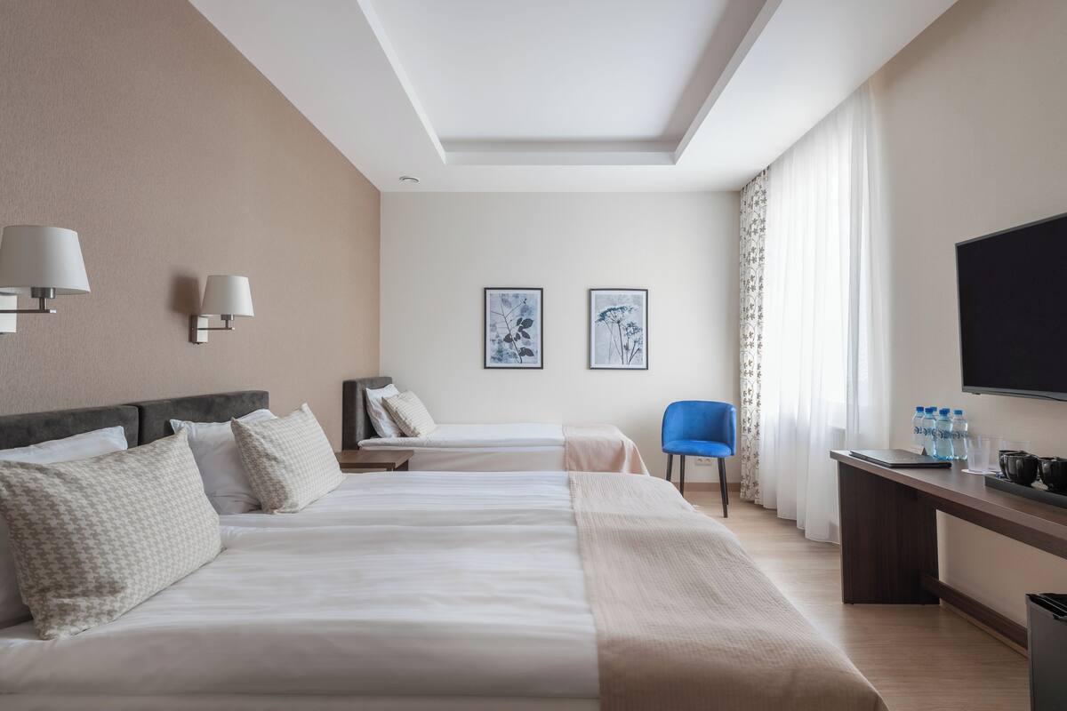 A hotel room with two beds, a desk, a chair, a TV, and artwork on the wall.