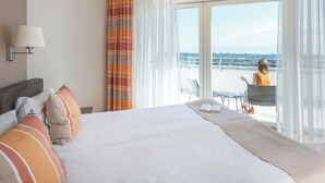 Une chambre d’hôtel avec un lit, une fenêtre avec des rideaux, une vue sur la ville et un balcon avec une chaise et une table.